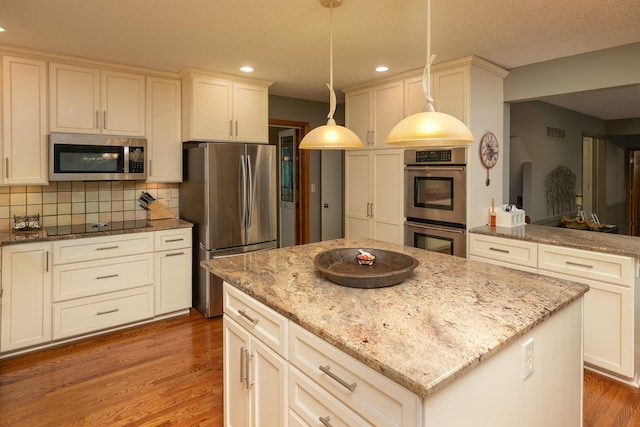 kitchen featuring wood-type flooring, appliances with stainless steel finishes, hanging light fixtures, light stone counters, and backsplash