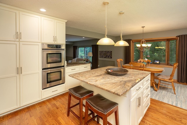 kitchen featuring white cabinetry, a kitchen breakfast bar, light wood-type flooring, stainless steel double oven, and a kitchen island