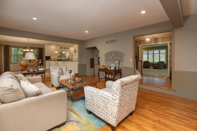 living room featuring light wood-type flooring, a notable chandelier, and a textured ceiling