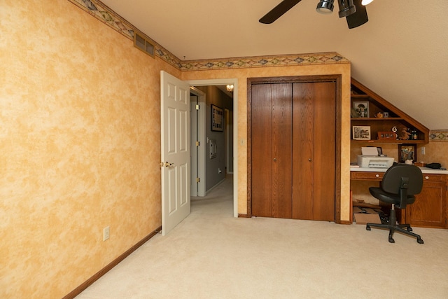 unfurnished office with vaulted ceiling, ceiling fan, built in shelves, and light colored carpet