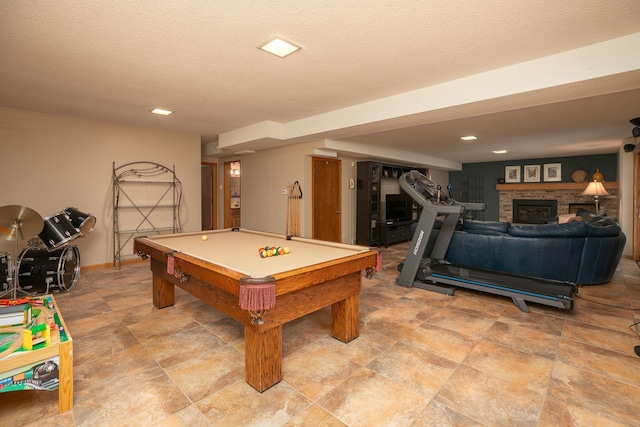 playroom with pool table, a textured ceiling, and a stone fireplace