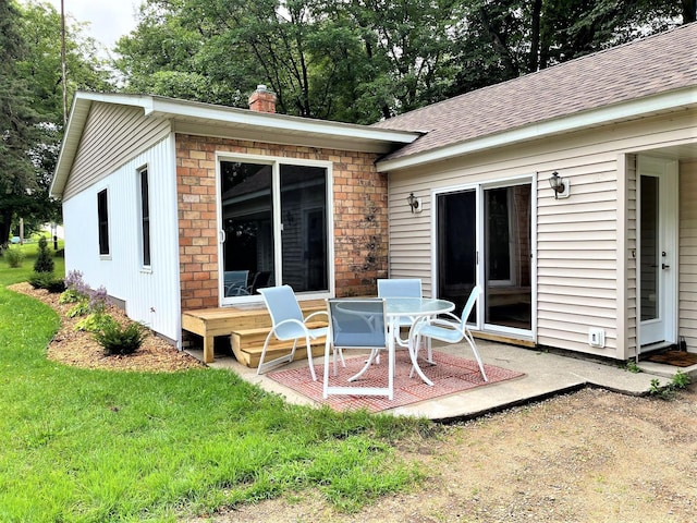 rear view of property featuring a patio area, a shingled roof, a chimney, and a yard