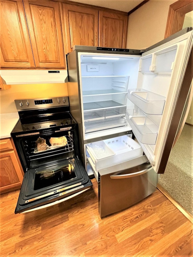 interior details featuring brown cabinetry, stainless steel electric range oven, light wood-style flooring, fridge, and under cabinet range hood