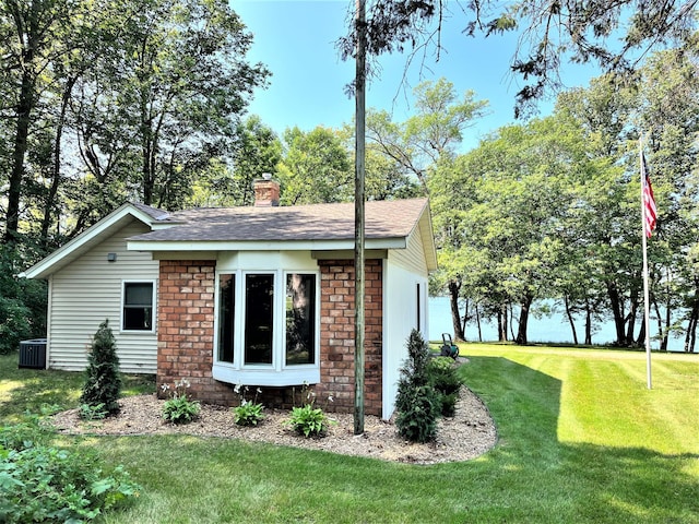 view of side of home featuring a chimney, central AC, a lawn, and brick siding