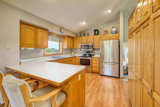 kitchen with appliances with stainless steel finishes, a sink, a kitchen breakfast bar, light countertops, and lofted ceiling