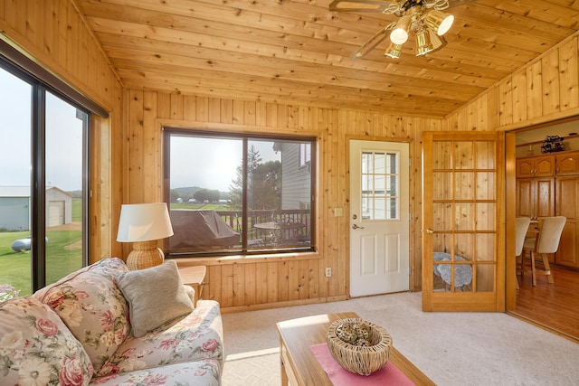 carpeted living area featuring lofted ceiling, healthy amount of natural light, wood walls, wooden ceiling, and a ceiling fan