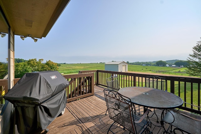 wooden terrace featuring a yard, an outbuilding, a rural view, outdoor dining area, and grilling area
