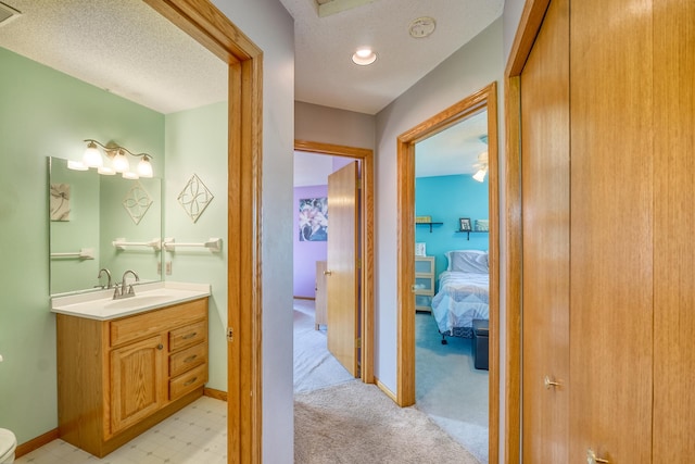 hallway with a sink, light colored carpet, baseboards, and a textured ceiling
