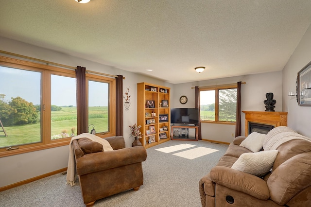 living area with carpet flooring, a textured ceiling, baseboards, and a glass covered fireplace