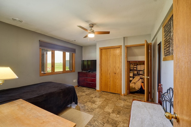 bedroom featuring a ceiling fan, stone finish floors, and two closets