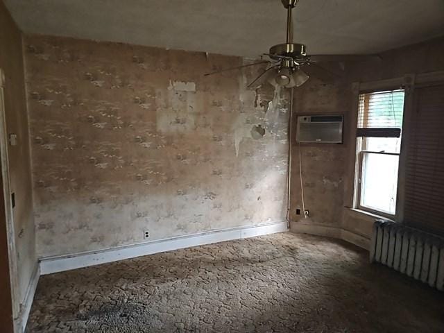 empty room with a wall mounted AC, carpet floors, radiator heating unit, and ceiling fan