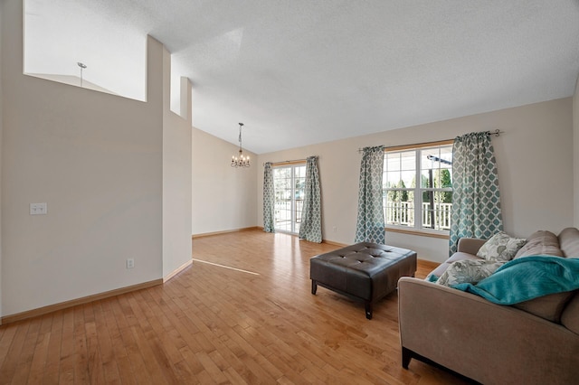 living area featuring a textured ceiling, a chandelier, baseboards, vaulted ceiling, and light wood finished floors