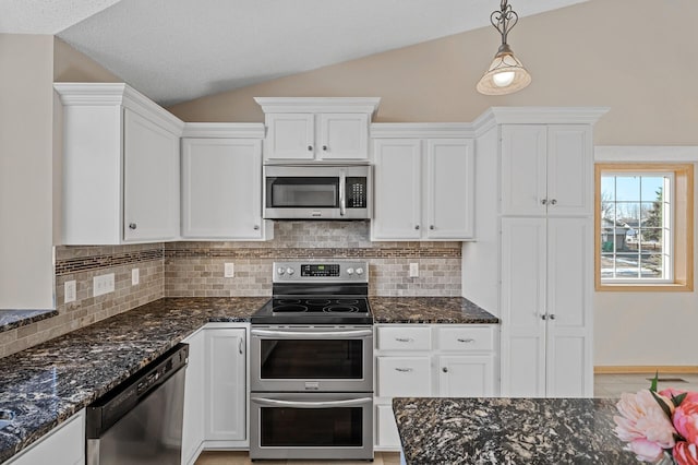 kitchen with pendant lighting, appliances with stainless steel finishes, white cabinets, vaulted ceiling, and dark stone counters