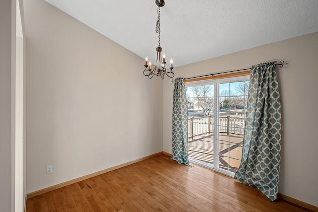 unfurnished room with an inviting chandelier, vaulted ceiling, a textured ceiling, baseboards, and hardwood / wood-style flooring