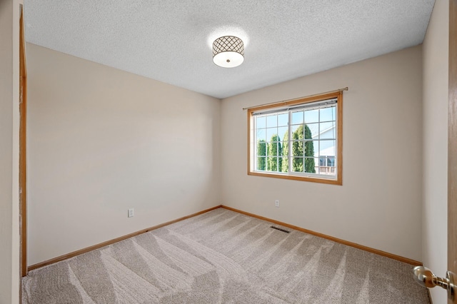 spare room with a textured ceiling, carpet flooring, visible vents, and baseboards