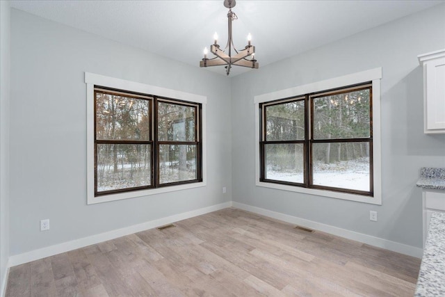 unfurnished dining area featuring plenty of natural light, a notable chandelier, and light wood-type flooring