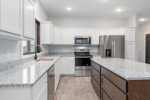 kitchen featuring stainless steel appliances, sink, white cabinets, light hardwood / wood-style floors, and a kitchen island