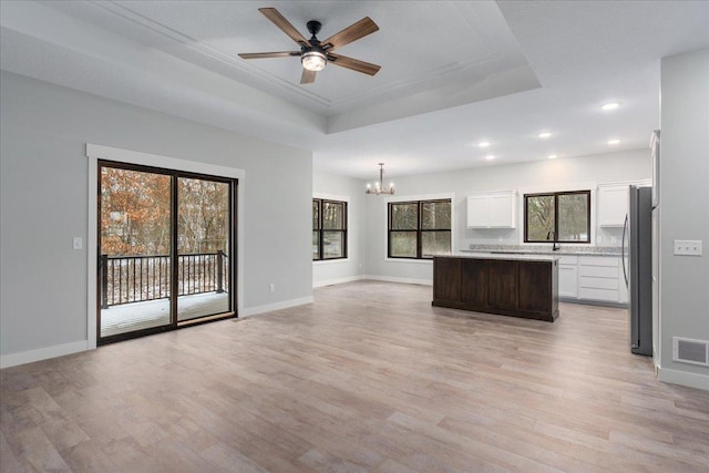 unfurnished living room with ceiling fan with notable chandelier, light hardwood / wood-style floors, a tray ceiling, and sink