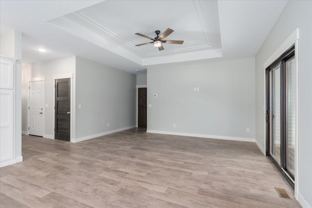 spare room with ceiling fan, a raised ceiling, and light wood-type flooring