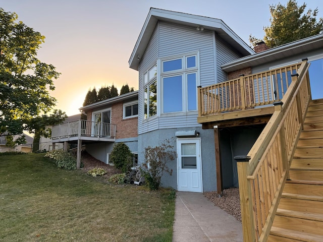 back house at dusk with a wooden deck and a yard