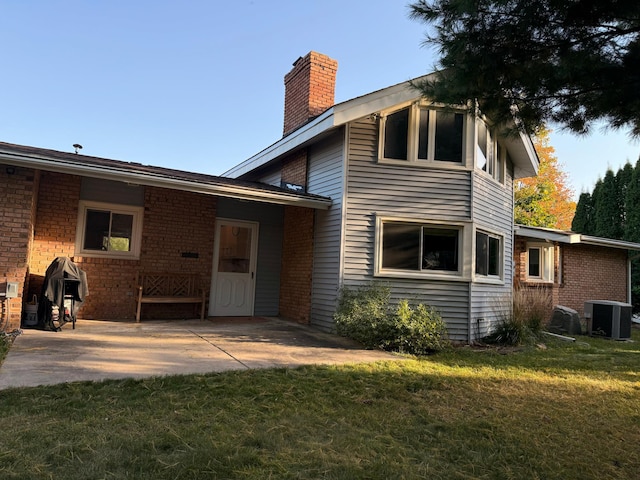 back of property with a patio, a lawn, and central AC