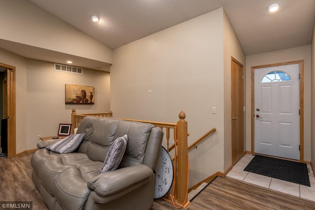 entryway with a textured ceiling, vaulted ceiling, and light hardwood / wood-style flooring