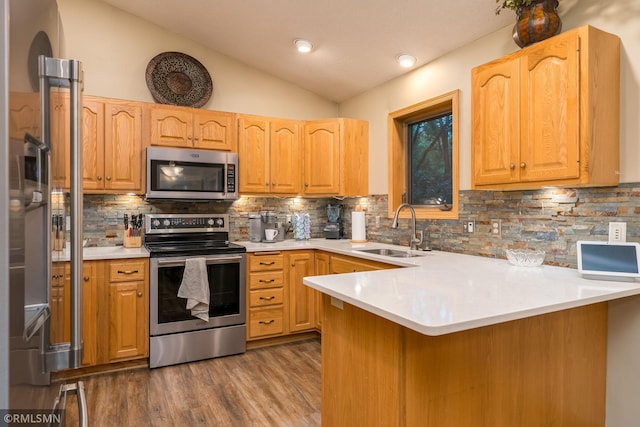 kitchen featuring appliances with stainless steel finishes, backsplash, kitchen peninsula, lofted ceiling, and sink