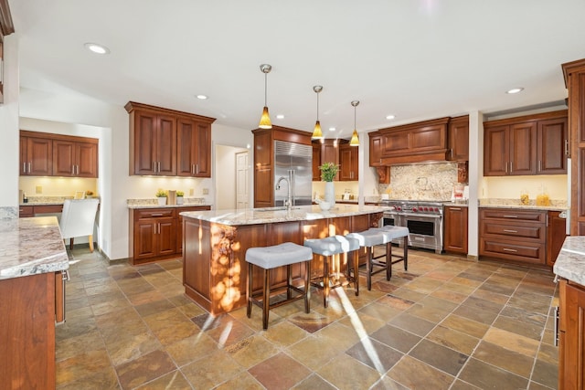 kitchen featuring a breakfast bar, pendant lighting, premium appliances, a kitchen island with sink, and light stone countertops