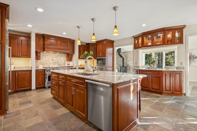 kitchen featuring decorative light fixtures, sink, light stone counters, stainless steel appliances, and a center island with sink