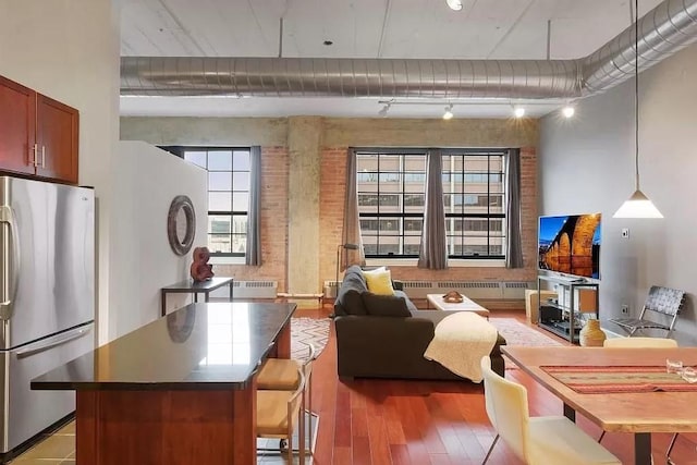 kitchen with track lighting, stainless steel fridge, a high ceiling, light wood-type flooring, and brick wall