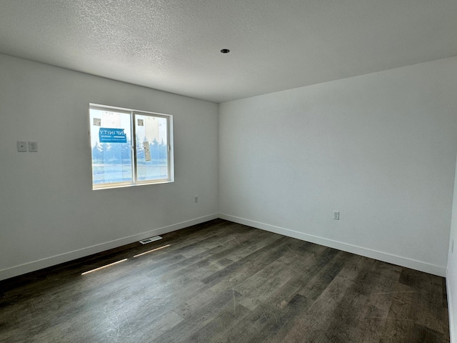 unfurnished room featuring visible vents, a textured ceiling, dark wood-type flooring, and baseboards