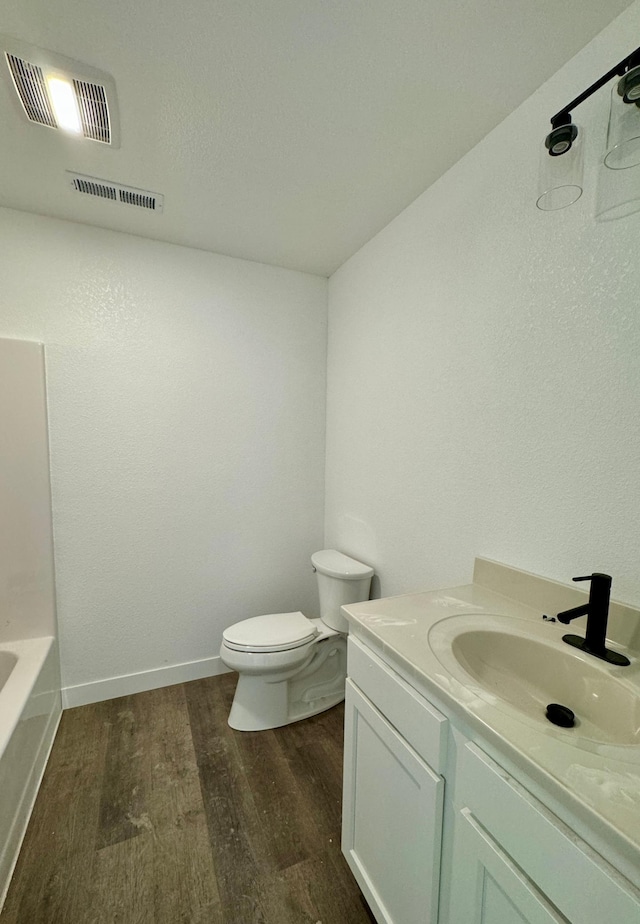 full bathroom with visible vents, toilet, a tub to relax in, wood finished floors, and vanity