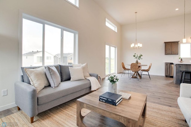 living room featuring light hardwood / wood-style flooring, a wealth of natural light, a chandelier, and a high ceiling