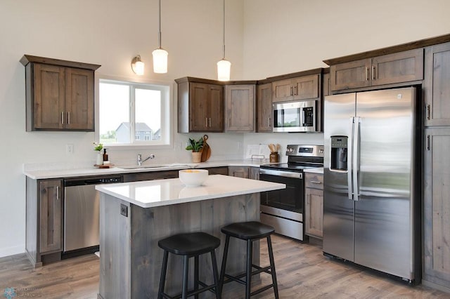 kitchen featuring sink, a towering ceiling, stainless steel appliances, a center island, and decorative light fixtures