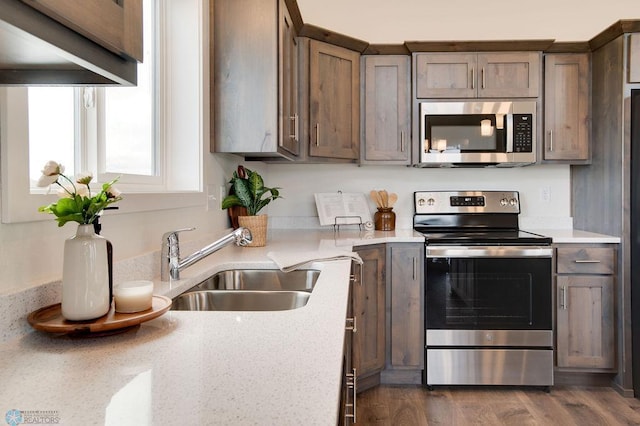 kitchen with dark wood-style floors, light stone countertops, stainless steel appliances, and a sink