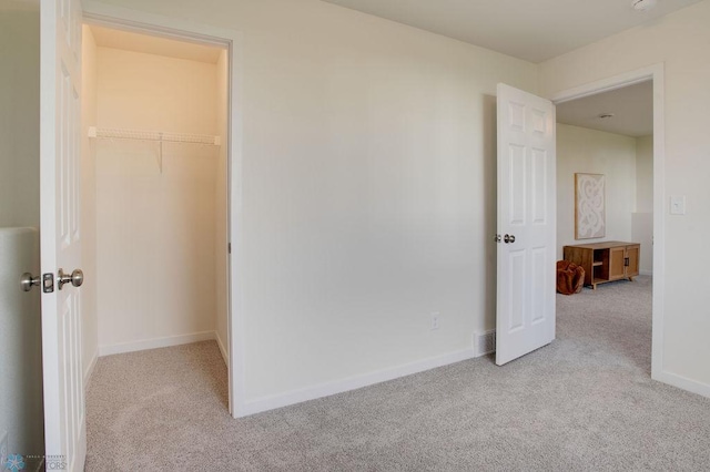 unfurnished bedroom featuring a closet, carpet flooring, a walk in closet, and baseboards