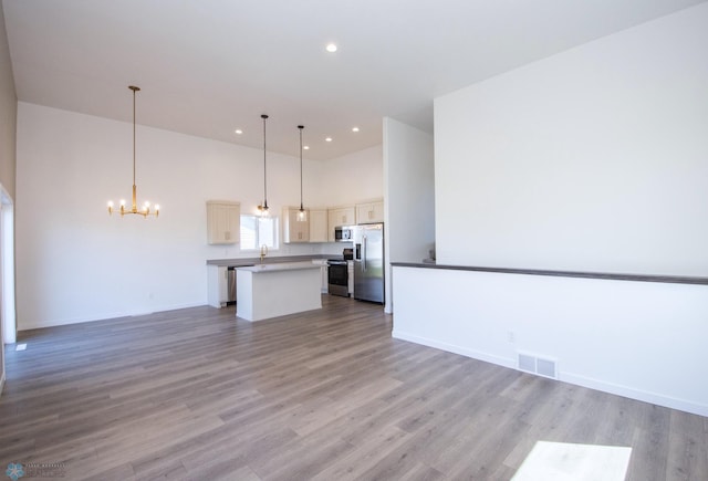 unfurnished living room featuring visible vents, a towering ceiling, a notable chandelier, and light wood-type flooring