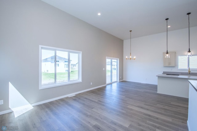 unfurnished living room featuring a high ceiling, an inviting chandelier, a sink, baseboards, and wood finished floors