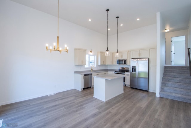 kitchen with an inviting chandelier, a center island, a sink, light wood finished floors, and appliances with stainless steel finishes
