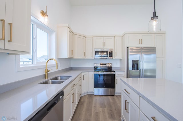 kitchen featuring hanging light fixtures, a sink, light countertops, stainless steel appliances, and white cabinetry