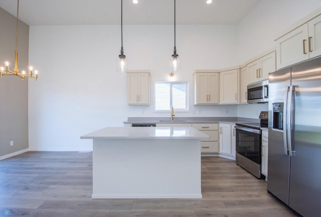 kitchen with an inviting chandelier, a sink, stainless steel appliances, wood finished floors, and a kitchen island