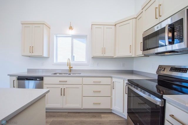 kitchen featuring appliances with stainless steel finishes, light wood-style flooring, a sink, light countertops, and white cabinetry