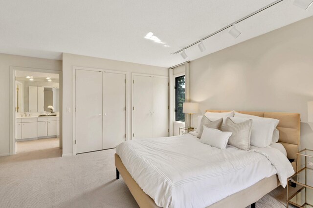 bedroom with ensuite bathroom, sink, multiple closets, rail lighting, and light carpet