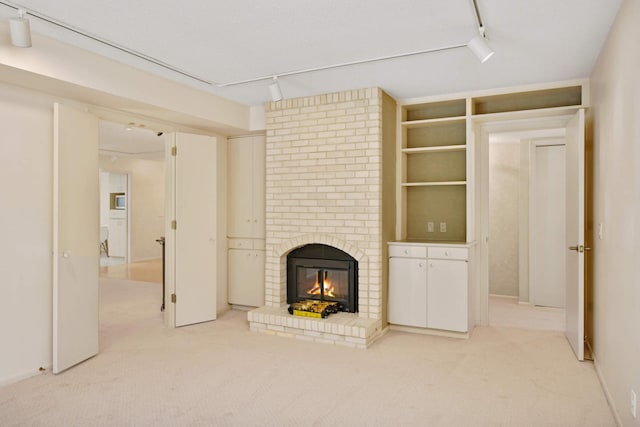 unfurnished living room featuring track lighting, a brick fireplace, and light colored carpet