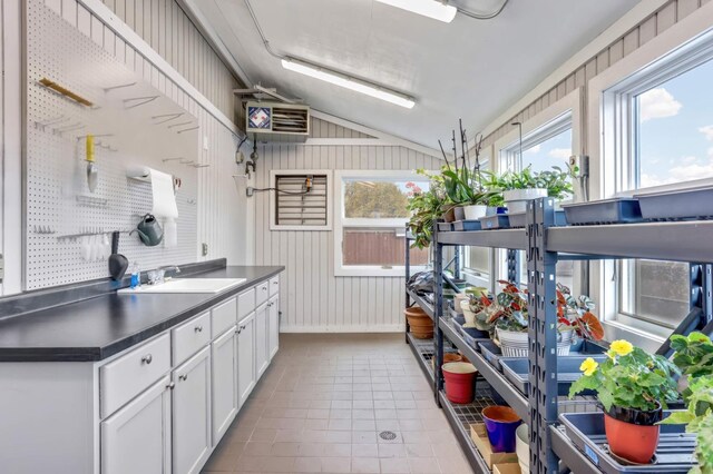 kitchen with wood walls, white cabinets, sink, and vaulted ceiling