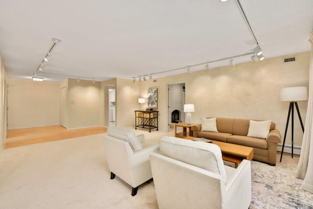 living room with baseboard heating, light hardwood / wood-style floors, a brick fireplace, and rail lighting