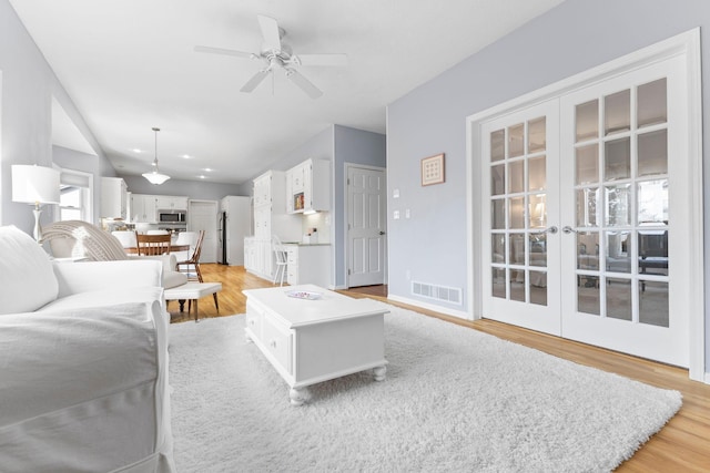 living room featuring visible vents, light wood finished floors, a ceiling fan, and french doors