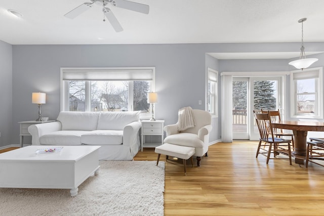 living room with baseboards, light wood-type flooring, and ceiling fan