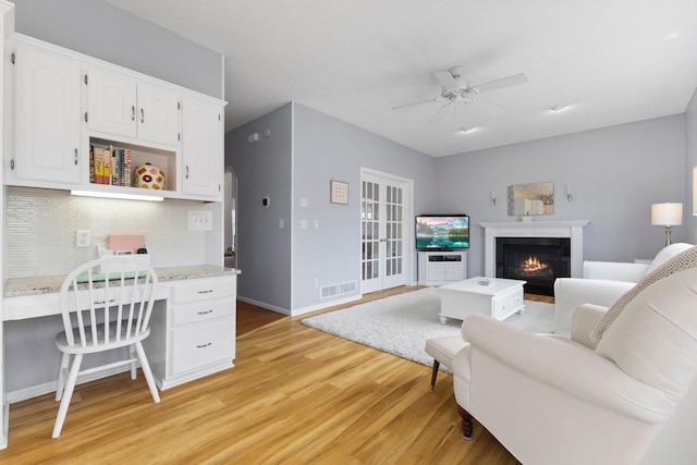 office with visible vents, light wood-style flooring, a glass covered fireplace, baseboards, and ceiling fan