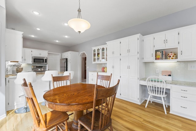 dining space featuring arched walkways, built in desk, recessed lighting, and light wood-type flooring